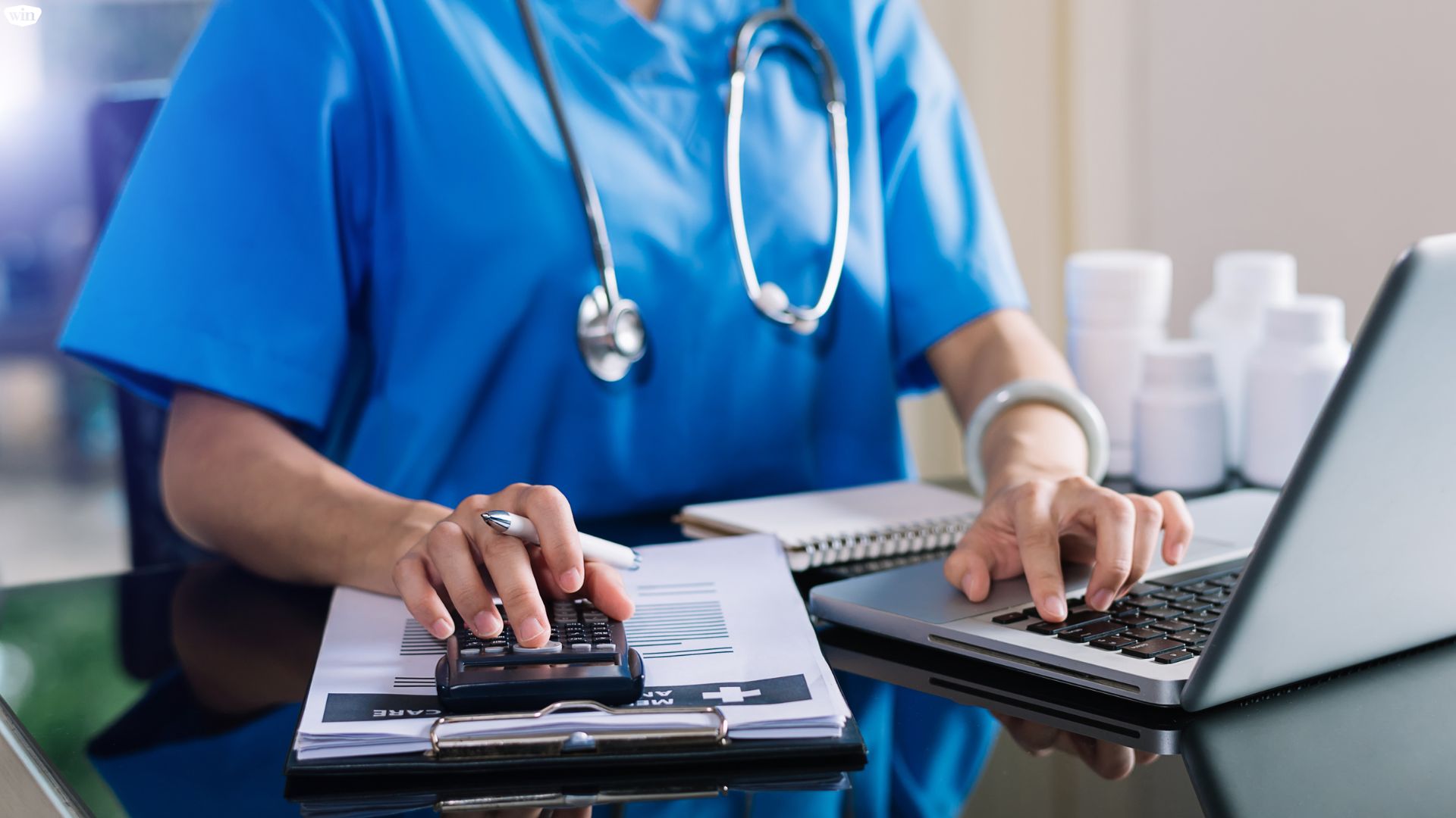 A healthcare provider working on a laptop and using a calculator