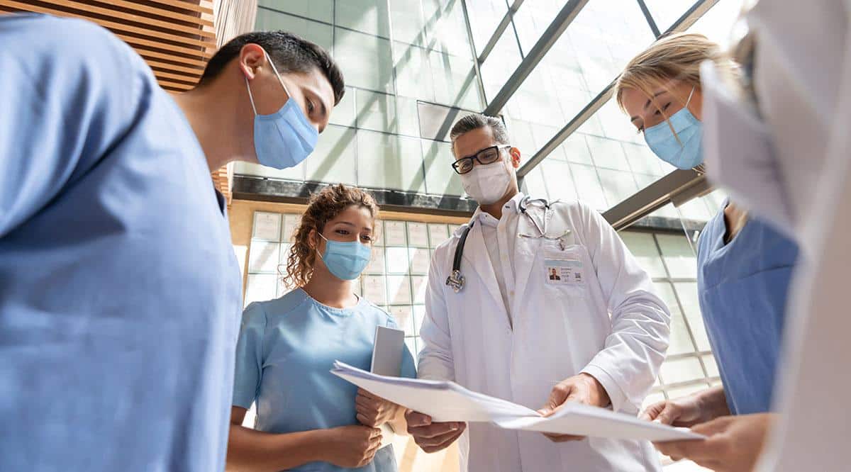 Healthcare providers standing in a circle reviewing documents