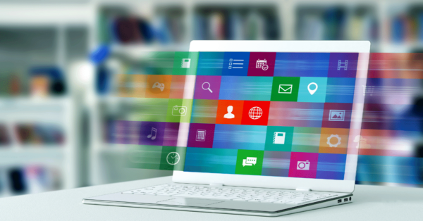 A laptop on a desk displaying colorful, transparent application icons floating above the screen